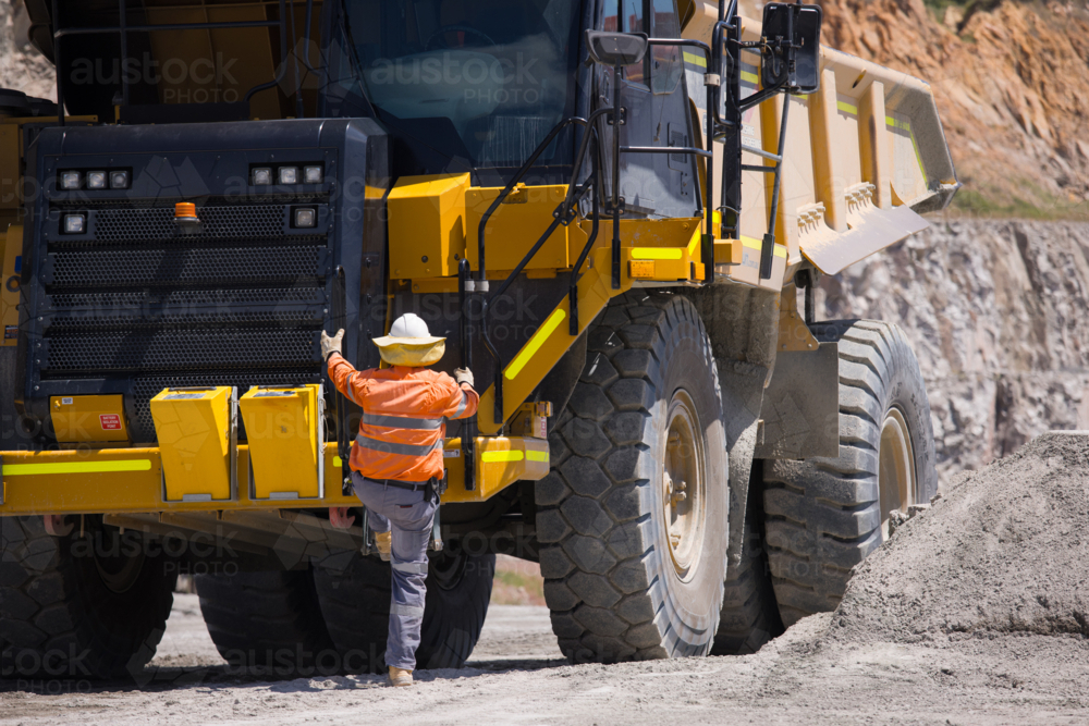 Man in high visibility clothes climbing up the dump truck. - Australian Stock Image