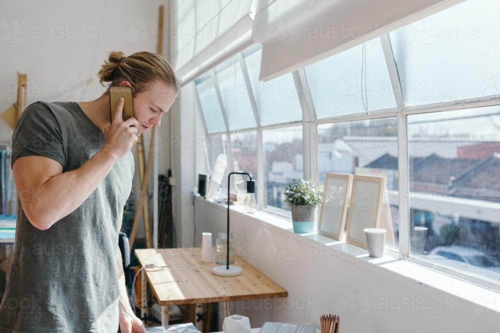 Man in his 20s on the phone in a creative studio office - Australian Stock Image