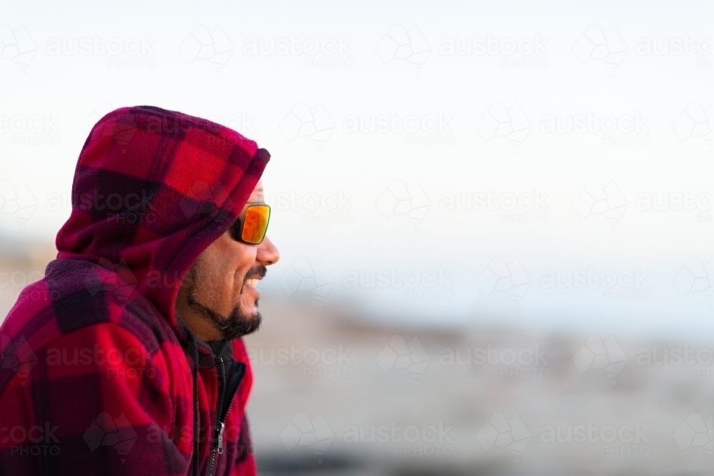 Man in red checked hoody with face in profile wearing sunnies - Australian Stock Image