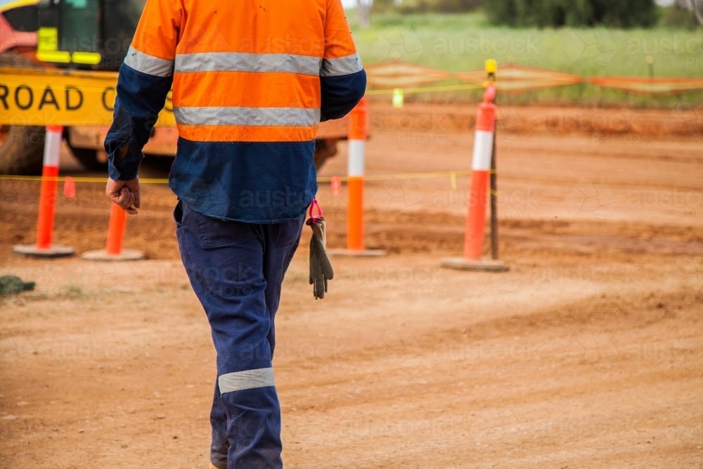 Man in reflective clothing walking around new road construction - Australian Stock Image