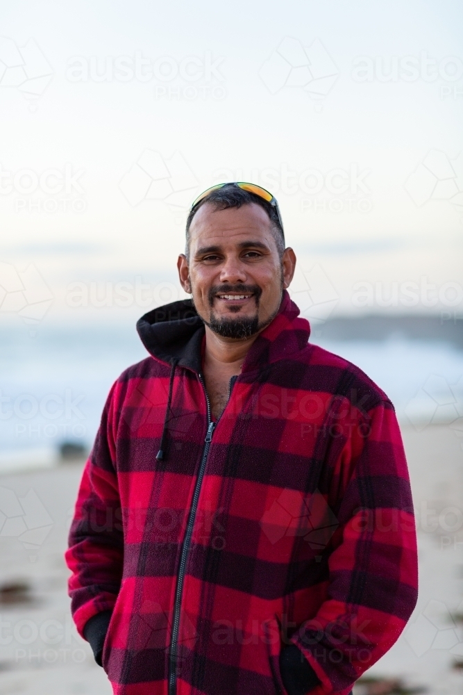 Man in warm checked jacket at beach with sunnies on head - Australian Stock Image