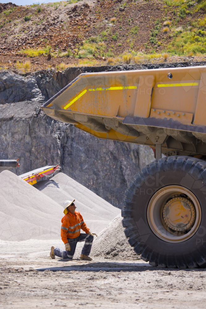 Man in workwear kneeling on the ground while checking the dump truck. - Australian Stock Image