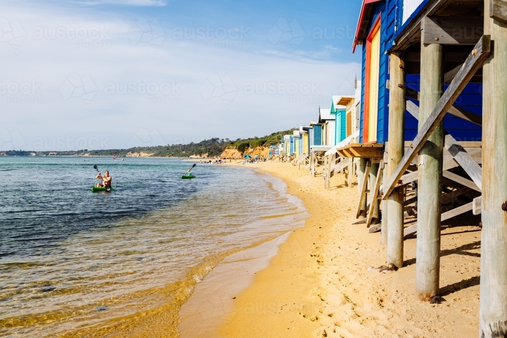 Man kayaking in the water at Mt Martha, with beach huts along the shore - Australian Stock Image