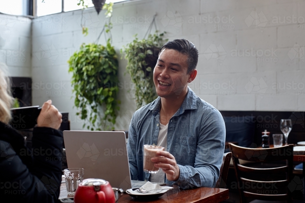 Man talking with friend whilst drinking coffee at cafe - Australian Stock Image
