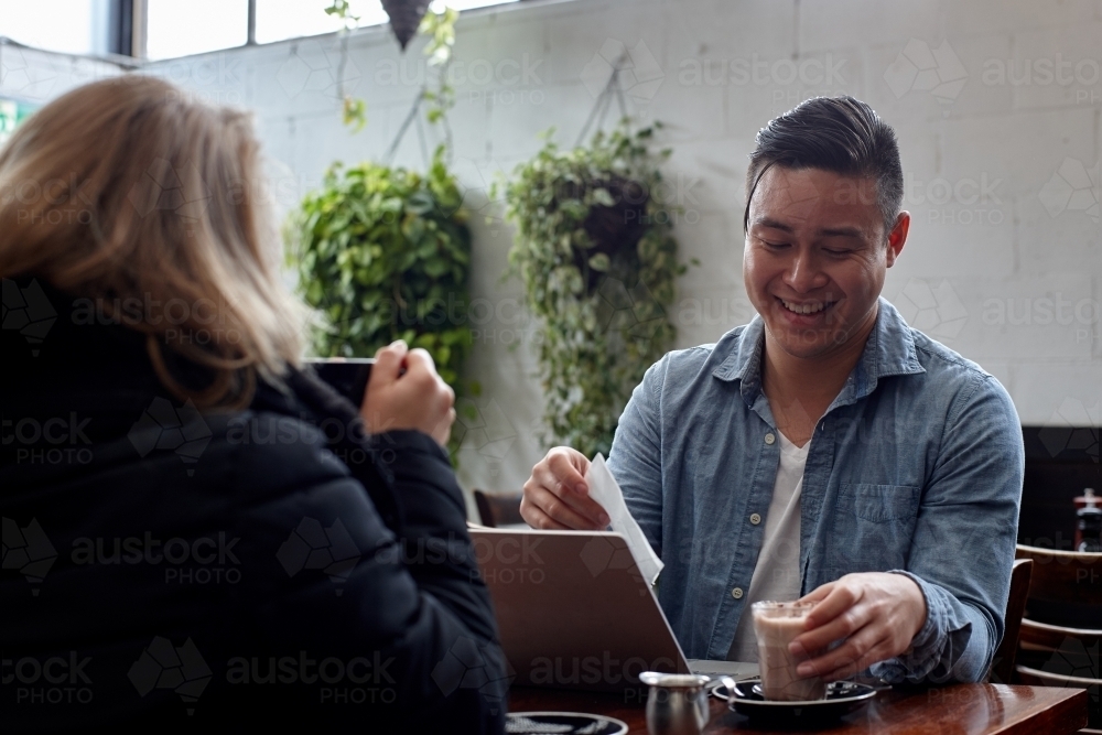 Man laughing over coffee at cafe with friend - Australian Stock Image