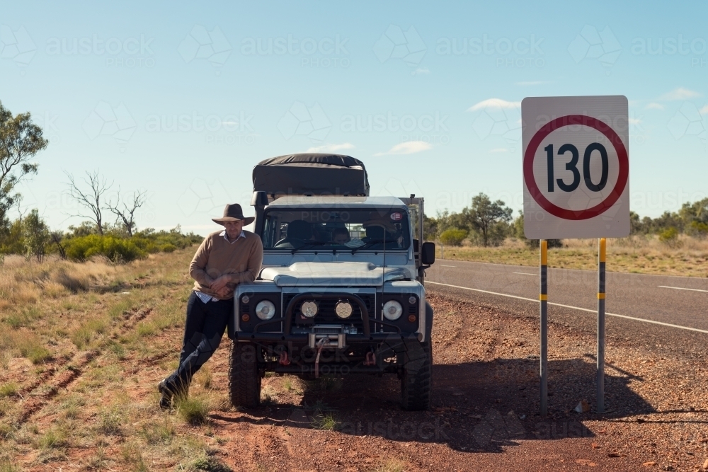 man leaning against his 4x4 car in outback NT, with road sign - Australian Stock Image