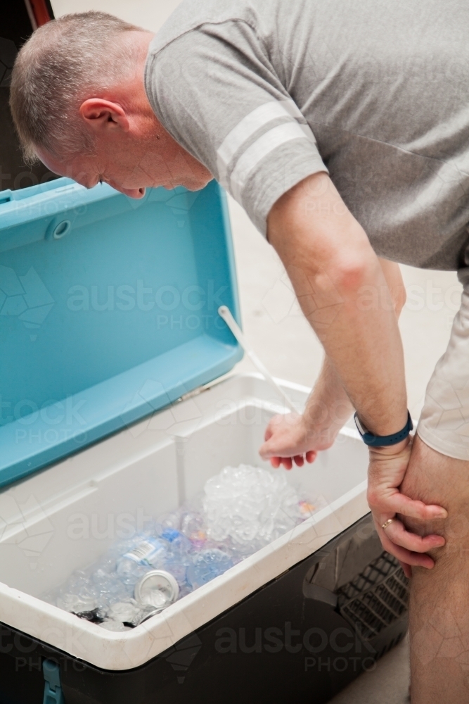 Man leaning down to a esky full of ice and drinks - Australian Stock Image