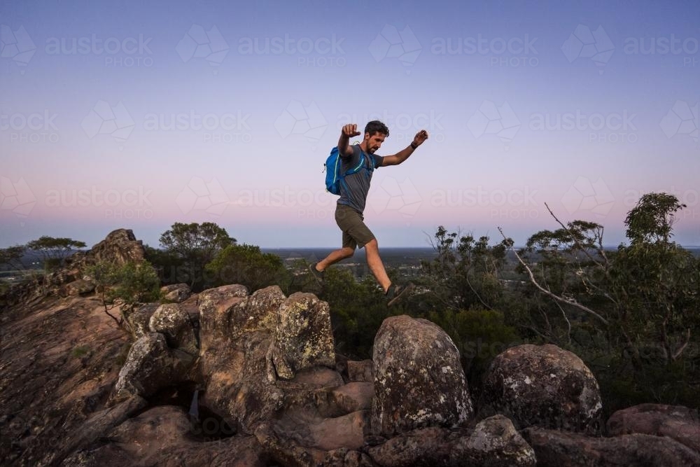 Image of Man leaping across rocks - Austockphoto