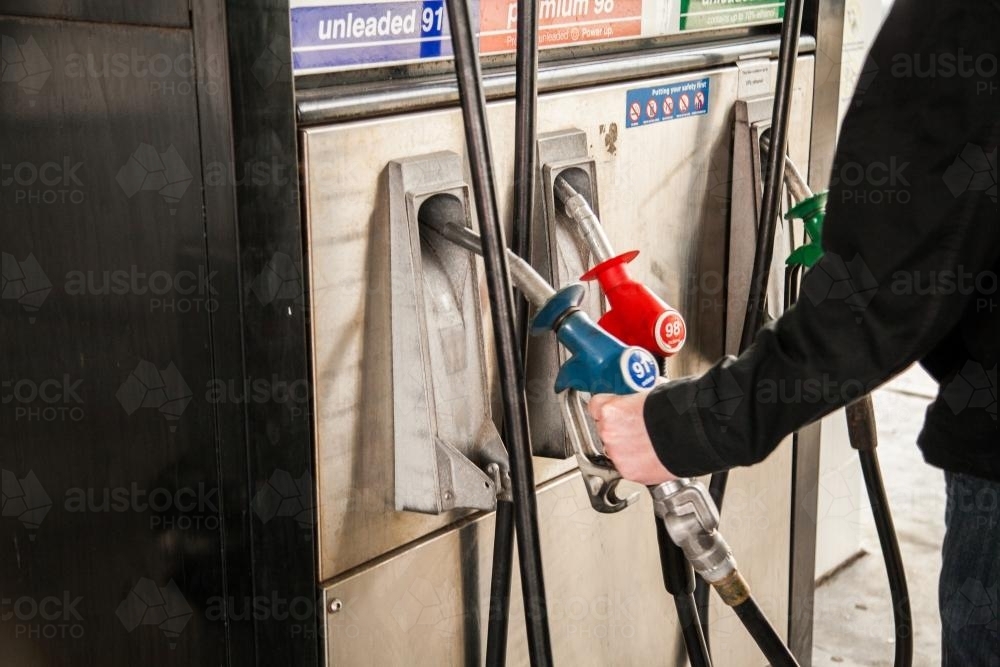 Man lifting petrol pump nozzle to fill up car with fuel - Australian Stock Image