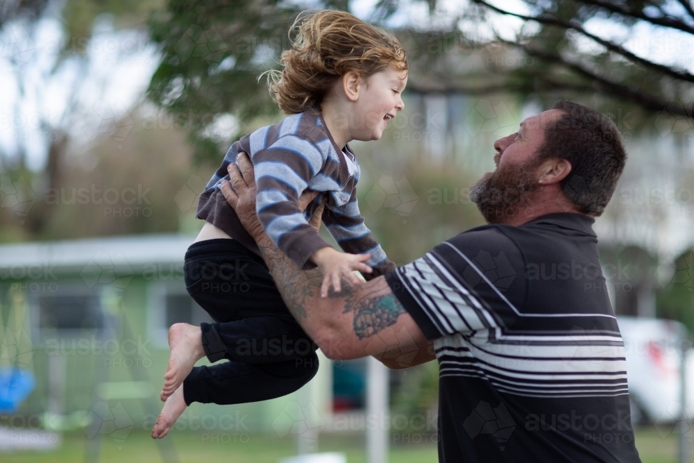 Man lifting young child in the air outside - Australian Stock Image