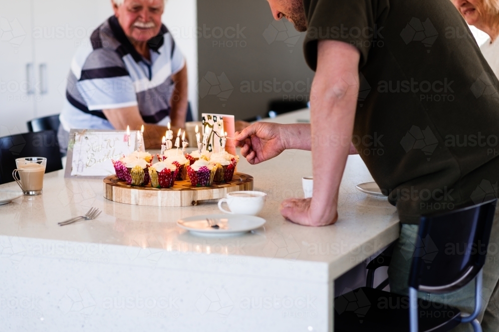 Man lighting candles on cupcakes for senior birthday party - Australian Stock Image