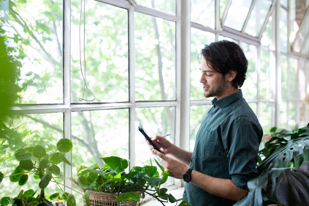 Man looking at device and thinking near glass windows - Australian Stock Image