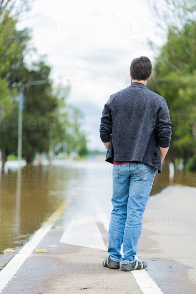 Man looking at floodwaters covering New England Highway road through singleton cutting off access - Australian Stock Image