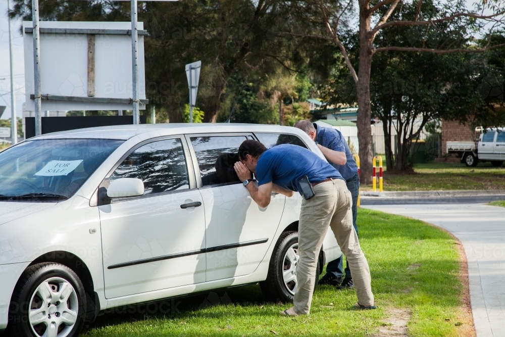 Man looking in window of car for sale by the side of the road - Australian Stock Image