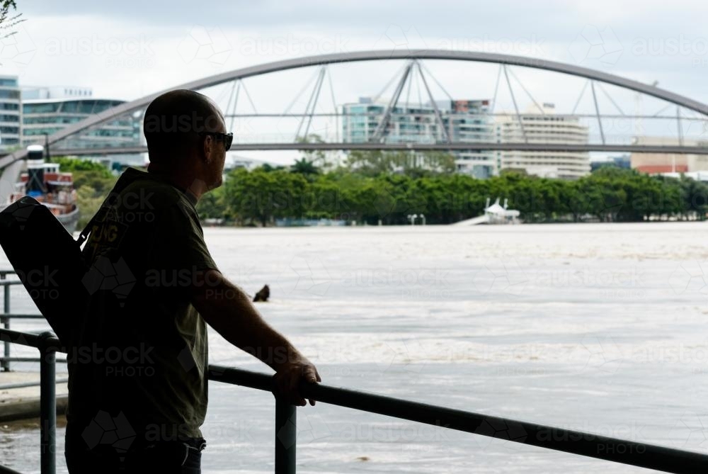 Man looking out on Flooded Brisbane River with Goodwill Bridge in background - Australian Stock Image