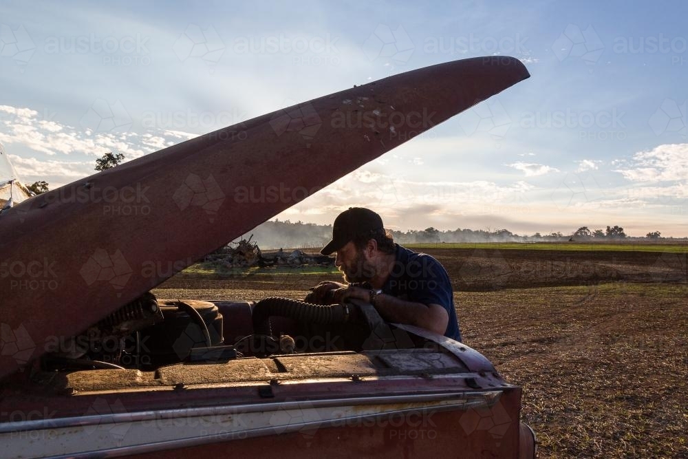Man looking under the bonnet of clapped out old truck - Australian Stock Image