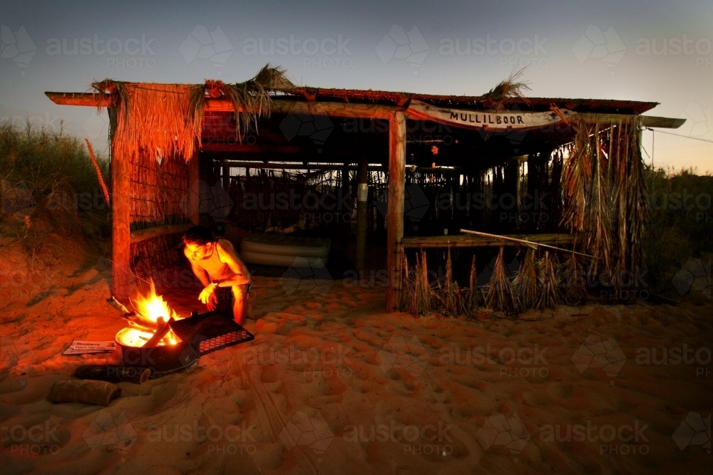 Man looks into campfire camping on a beach - Australian Stock Image