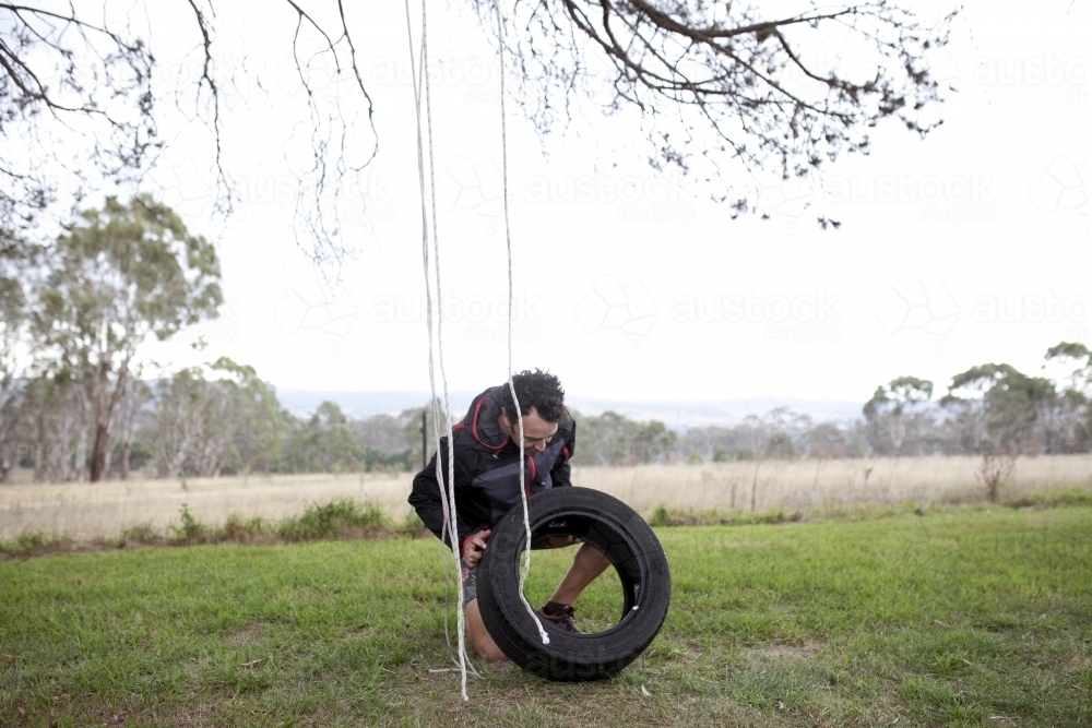 Man making a tyre swing in country backyard - Australian Stock Image
