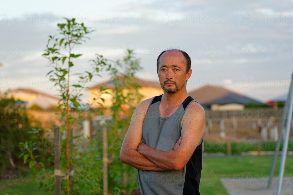Man of mixed race standing with crossed arms in a park at sunset - Australian Stock Image