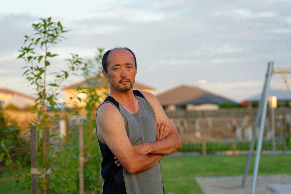 Man of mixed race standing with folded arms at sunset in a park - Australian Stock Image