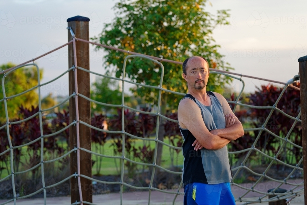 Man of mixed race standing with folded arms at sunset in a park - Australian Stock Image
