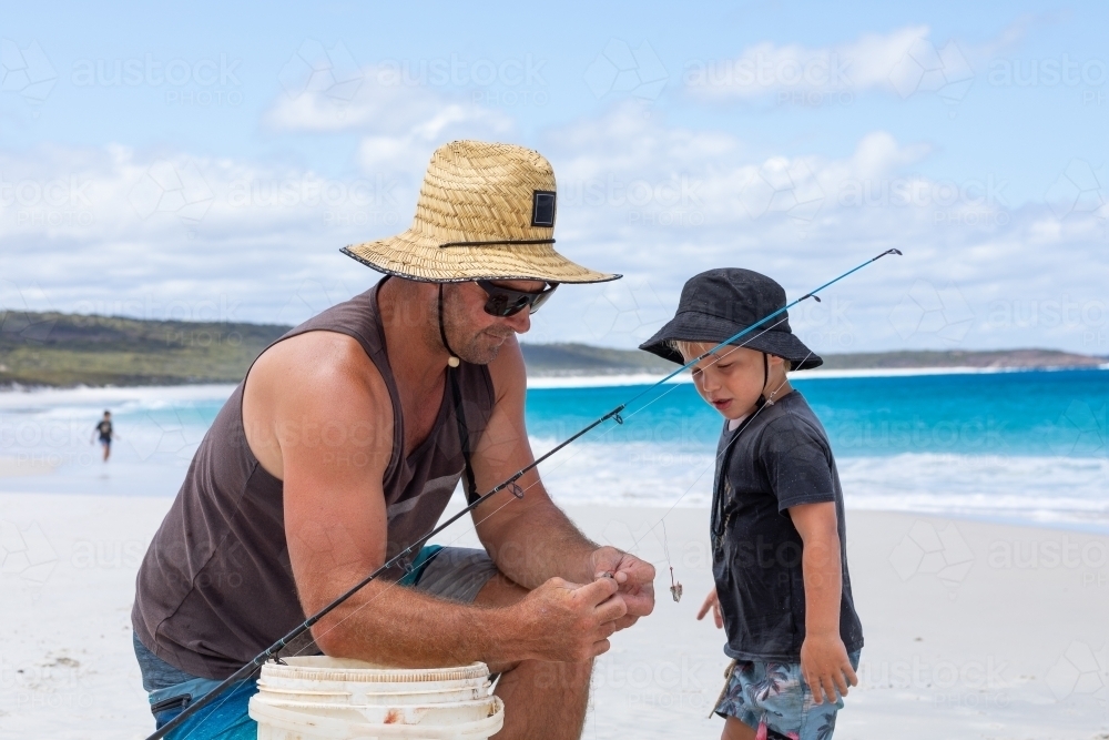 man on beach with young son putting bait on fishing hook - Australian Stock Image