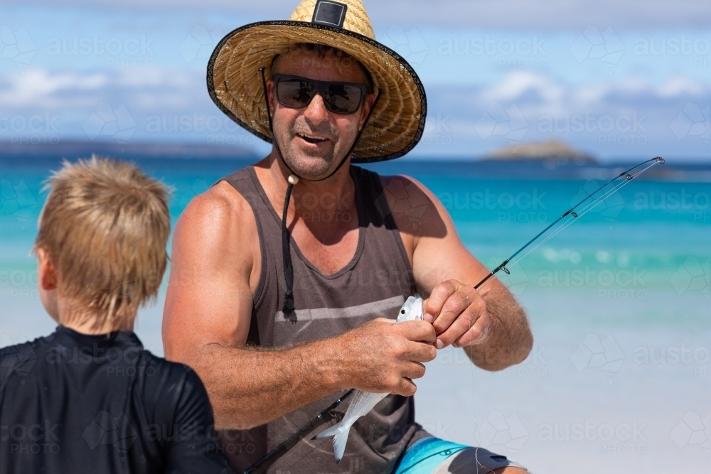 man on beach with young son putting bait on fishing hook - Australian Stock Image