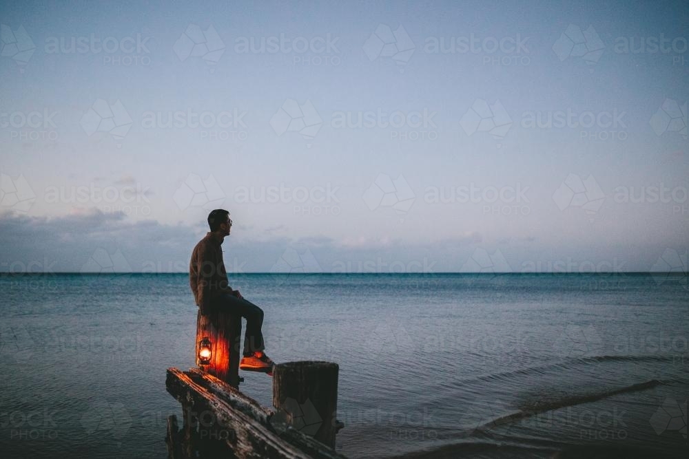 Man on old wooden jetty with lamp at dusk - Australian Stock Image