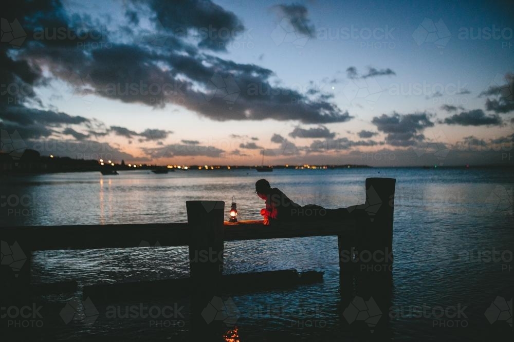 Man on old wooden jetty with lamp at dusk - Australian Stock Image