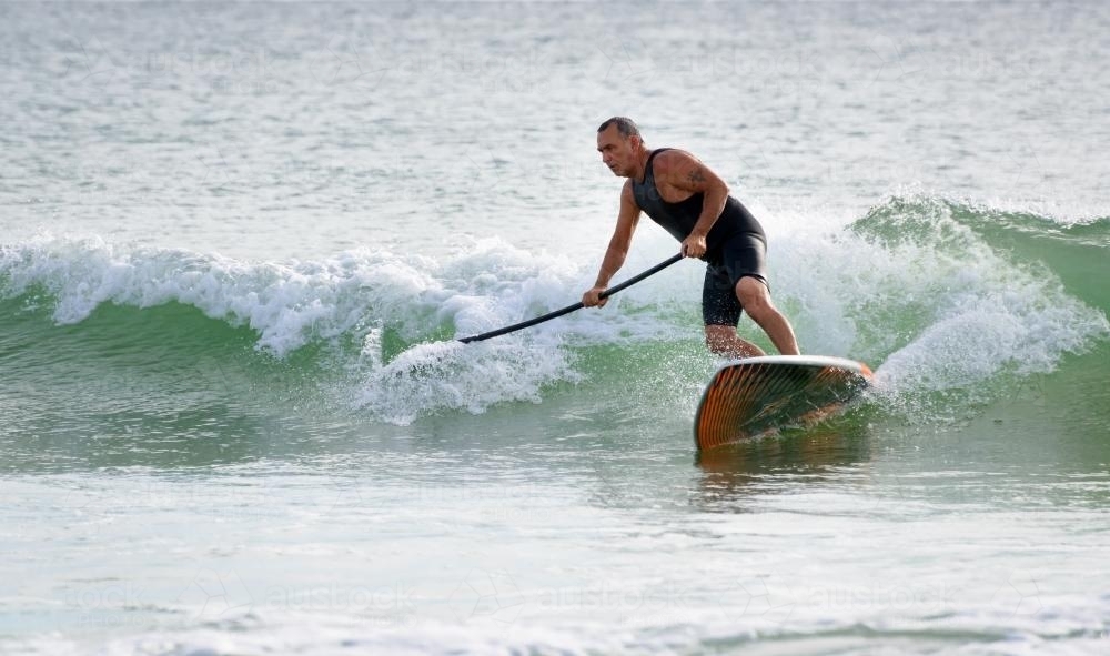 Man on paddleboard riding wave - Australian Stock Image