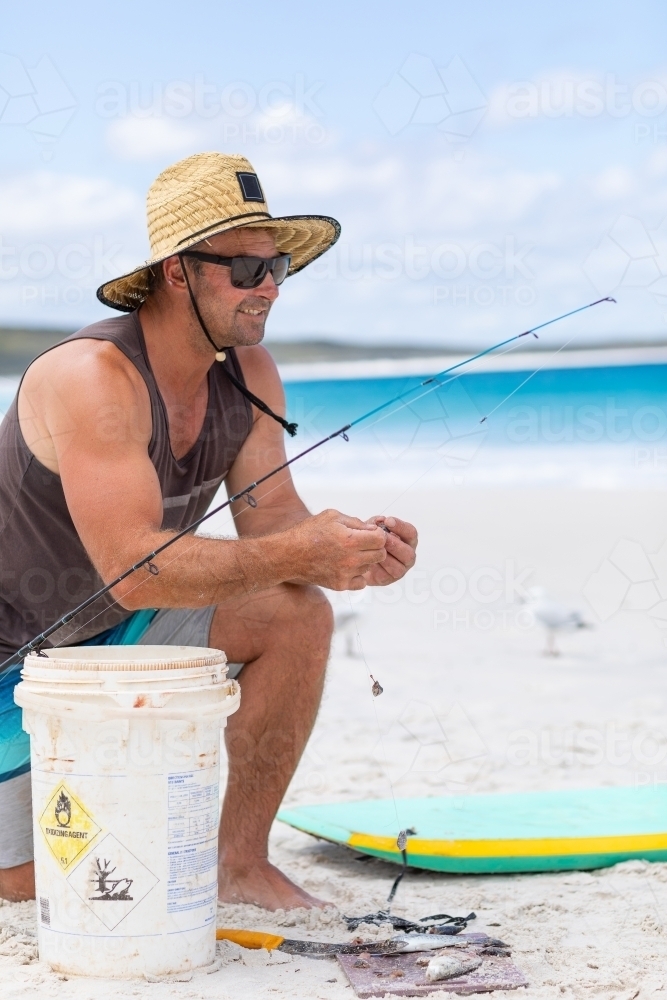 man on white sand beach kneeling down baiting fishing line - Australian Stock Image