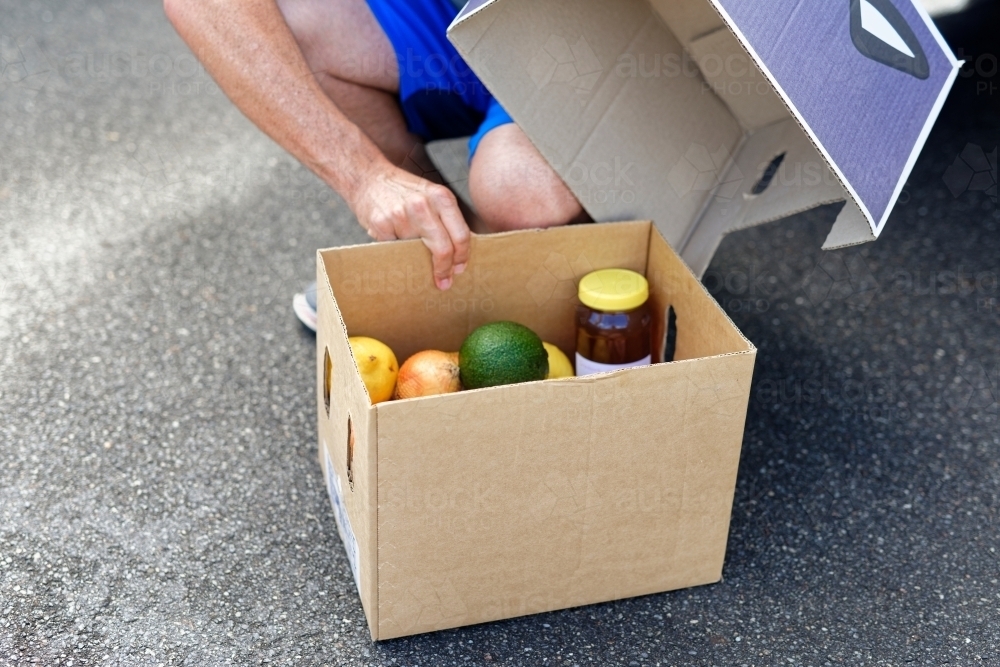 Man opening a box of fresh produce containing honey and avocado - Australian Stock Image