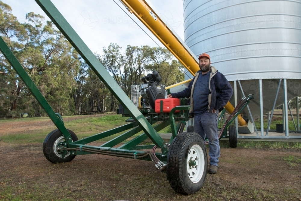 Man operating auger out of silo - Australian Stock Image