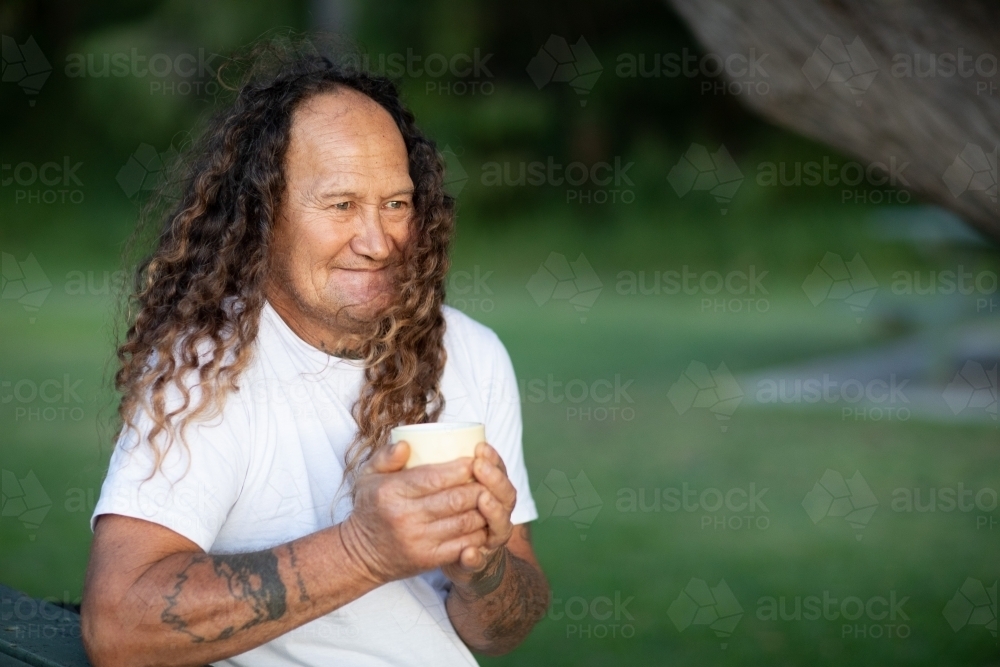 man outdoors in park holding cup in hands - Australian Stock Image
