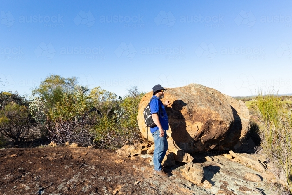man outdoors in the countryside near a large boulder - Australian Stock Image