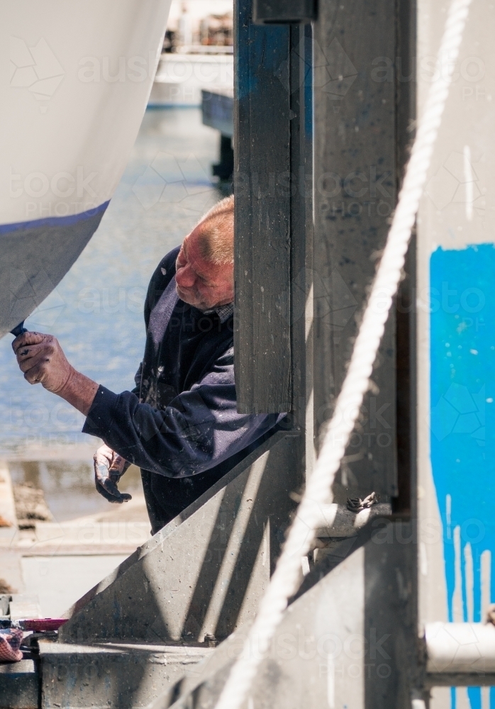 Man paints a boat in dry dock on the waters edge - Australian Stock Image
