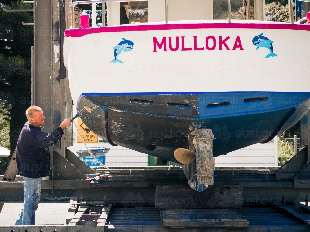Man paints underneath boat in dry dock - Australian Stock Image