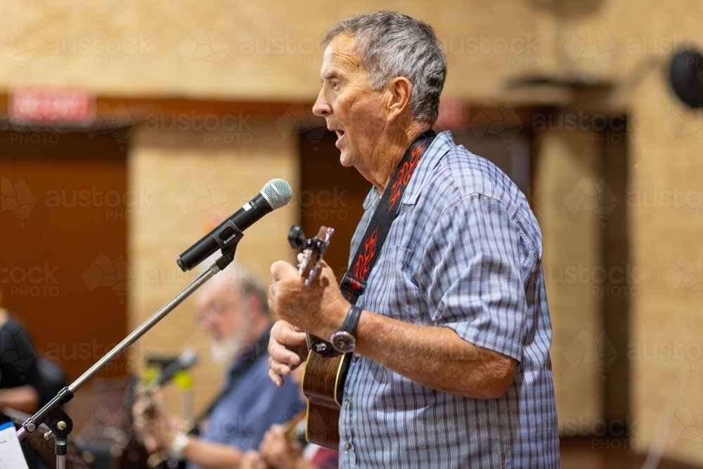man playing ukulele and singing into microphone - Australian Stock Image