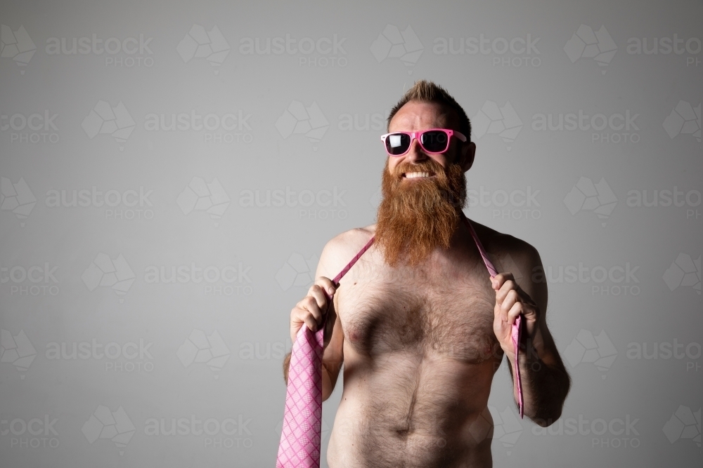 Man posing for photographs, shirtless with a pink tie and sunglasses - Australian Stock Image