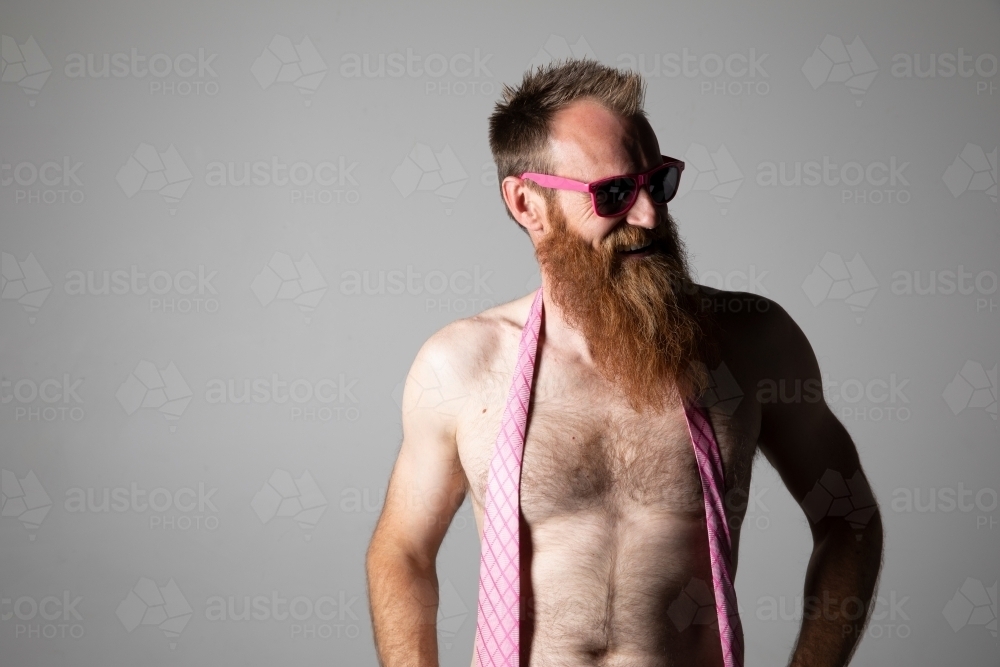 Man posing for photographs, shirtless with a pink tie and sunglasses - Australian Stock Image