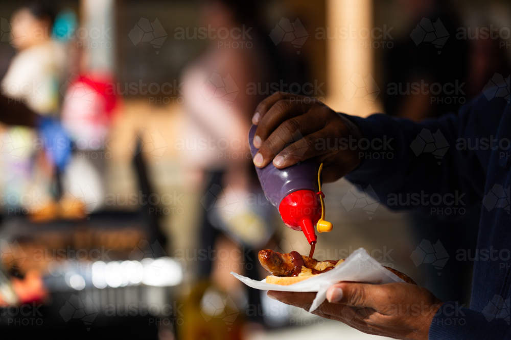 Man pouring bbq sauce at on sausage and bread held in hand on election day - Australian Stock Image