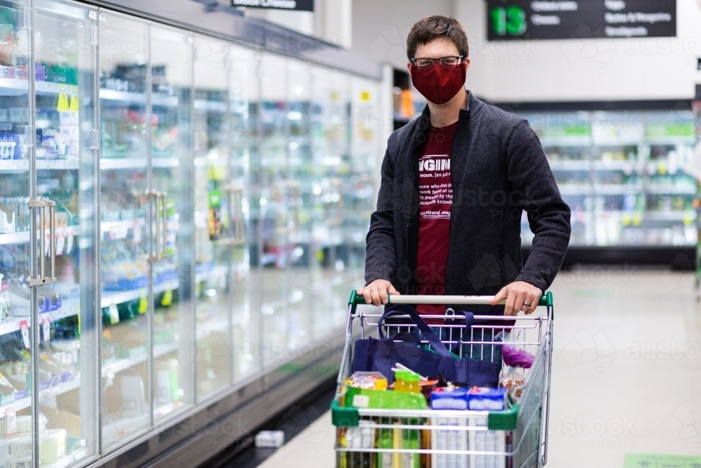 Man pushing shopping trolley doing the groceries for the family, and wearing a face mask - Australian Stock Image