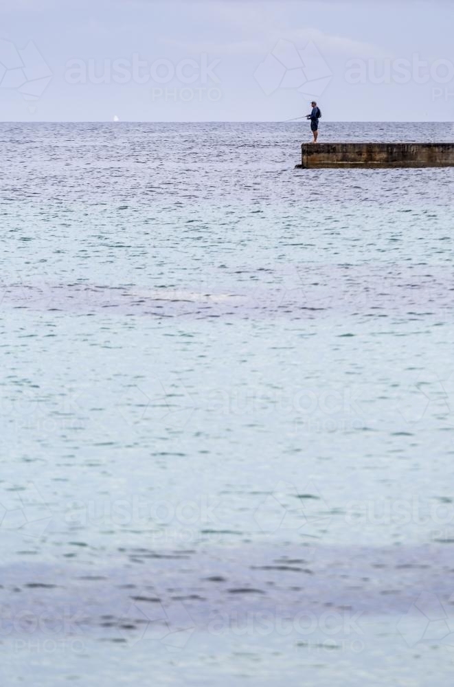 Man recreational fishing on the end of a concrete pier - Australian Stock Image