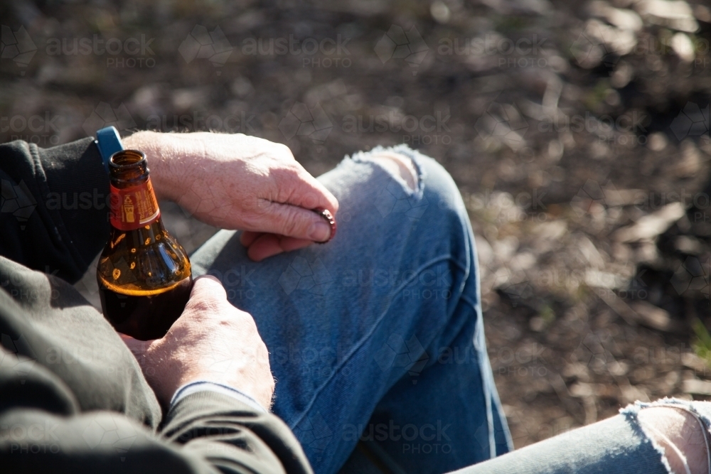 Man relaxing outside holding a bottle of beer - Australian Stock Image