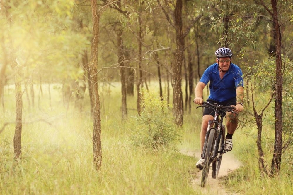 Man riding his pushbike on a dirt track among trees - Australian Stock Image