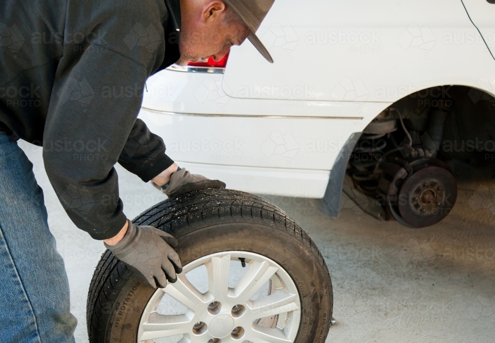 Man rolling flat tyre away from car to fix it - Australian Stock Image