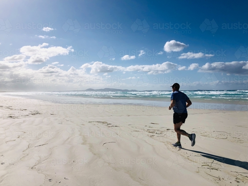 Man running on long white sandy stretch of beach - Australian Stock Image