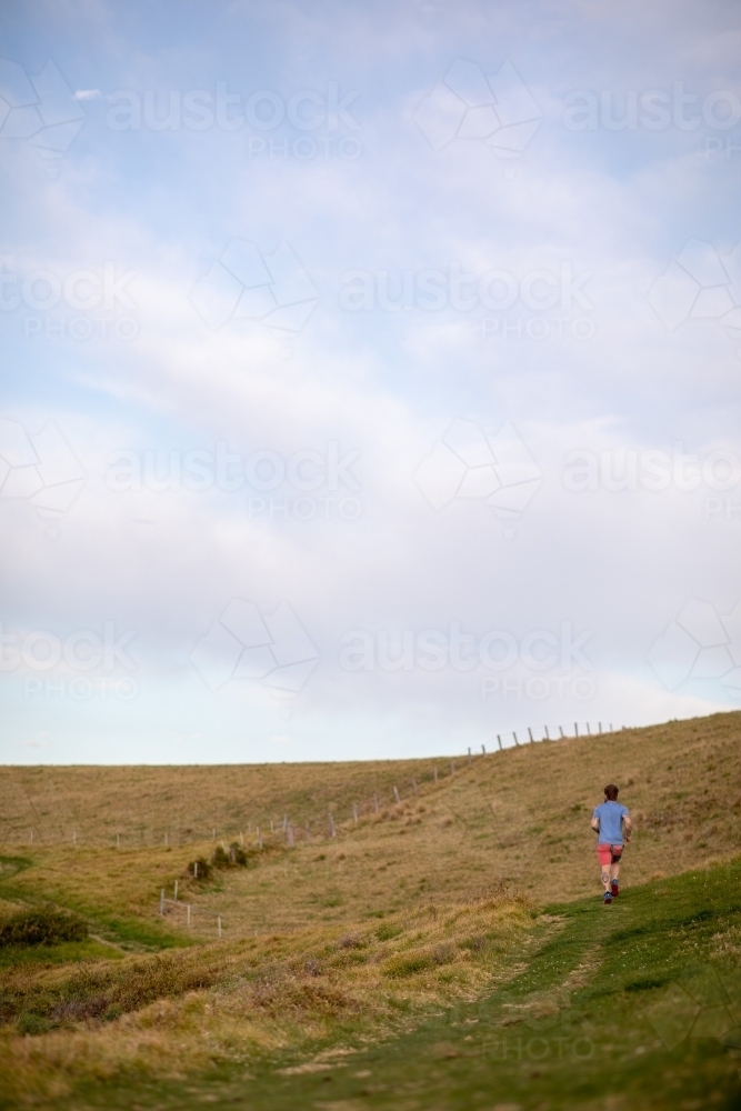 Man Running Uphill From Distance Under Blue Sky - Australian Stock Image