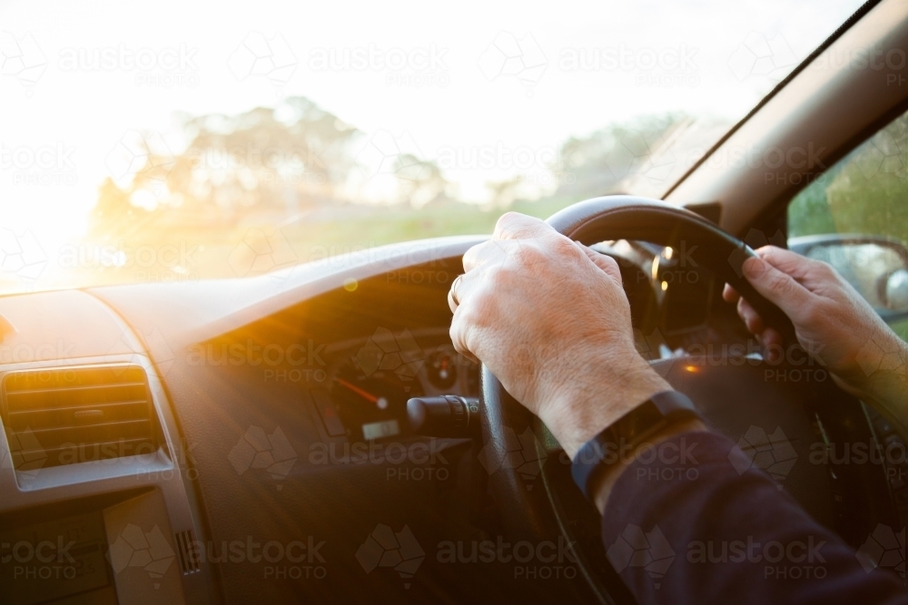 Man's hands on a car steering wheel with sun flare - Australian Stock Image