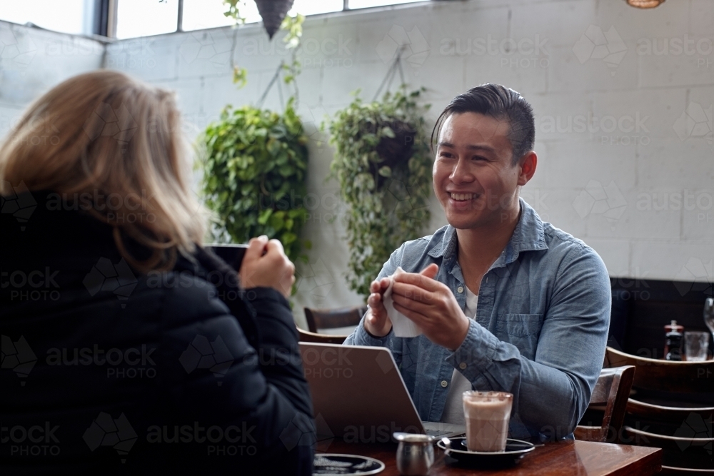 Man seated at table at cafe talking with friend - Australian Stock Image